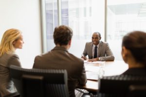 Friendly, Black, male lawyer meeting with clients at his desk.