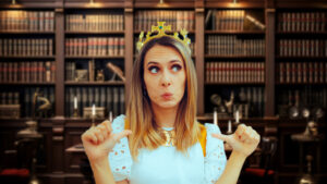 White woman in a white dress with crown on her head, pursed lips, and thumbs pointed at herself, standing in an empty law office